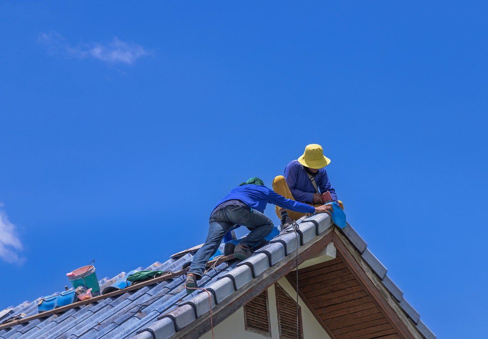 Workers Repairman repairing leaking ridges tile roofing and replace cracked broken tile roofing on blue sky background.