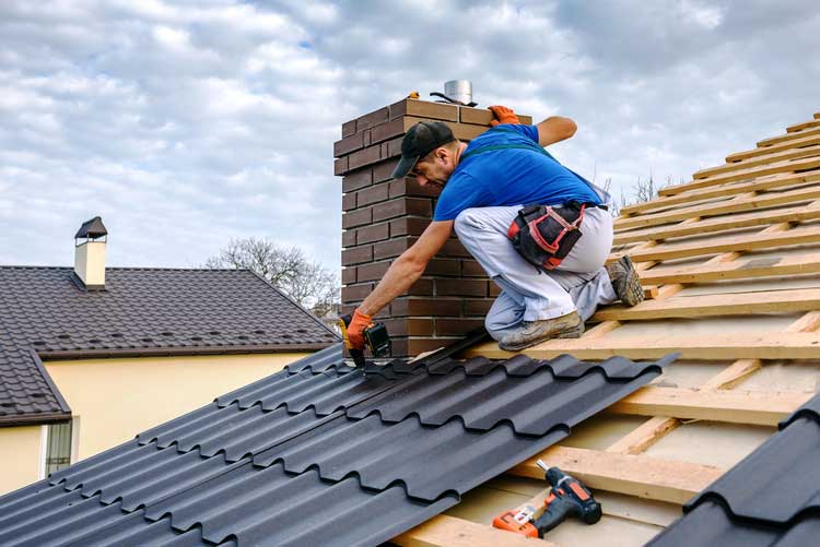 A man installs metal roofing on a house, carefully working on the sloped surface of the roof.